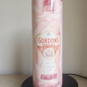 May include: A pink tumbler with a watercolour design of a Gordon's Premium Pink Distilled Gin bottle. The tumbler displays the brand's logo and the text "ESTD LONDON 1769". The background has a soft, pink watercolour effect.