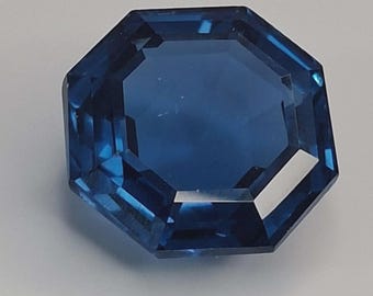 Peut inclure: Une pierre précieuse octogonale, taillée à facettes, d'un bleu profond. Les facettes réfléchissent la lumière, créant un éclat brillant. Cette gemme pourrait être un saphir, idéale pour la joaillerie.