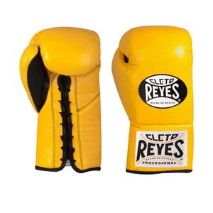 May include: A pair of bright yellow boxing gloves. The gloves have black accents and laces. The brand name "CLET0 REYES" is displayed on the gloves in a black oval with white text. The bottom of the glove has the text "HECHO EN MEXICO PROFESIONAL".