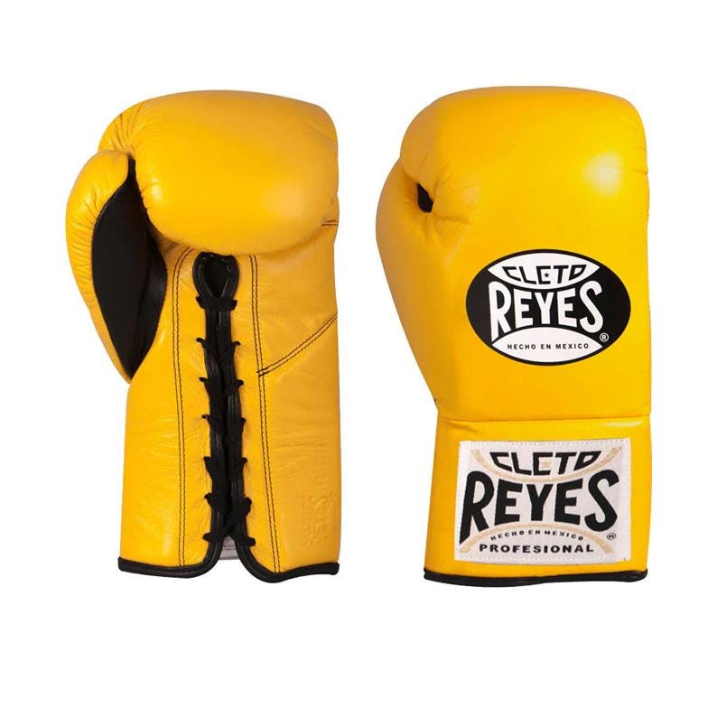 May include: A pair of bright yellow boxing gloves. The gloves have black accents and laces. The brand name "CLET0 REYES" is displayed on the gloves in a black oval with white text. The bottom of the glove has the text "HECHO EN MEXICO PROFESIONAL".