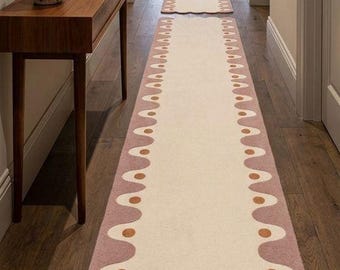 May include: Two matching hallway runners with a cream-colored center and a mauve border with copper-colored accents. The runners are placed on a dark wood floor in a hallway with neutral-colored walls.