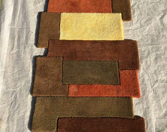 May include: A geometric rug with a patchwork design. The rug features rectangular and square shapes in shades of brown, orange, and yellow. The rug is made of a soft, textured material, and is suitable for a living room or bedroom.