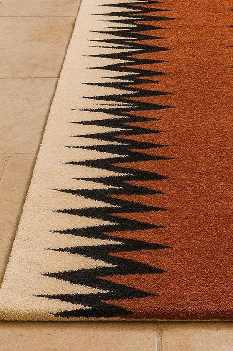 May include: A rectangular rug with a geometric design. The rug features a cream-colored section on the left, transitioning to a brown hue on the right. Black zigzag patterns run across the rug, creating a striking visual contrast.