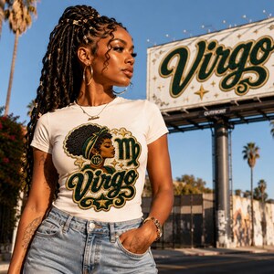 Può includere: Una t-shirt bianca a maniche corte con una stampa grafica di una persona con acconciatura afro, che indossa una fascia verde e oro, con il testo Virgo e il simbolo zodiacale della Vergine in un carattere corsivo decorativo verde e oro.