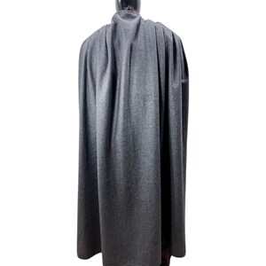 Puede incluir: Una capa larga y gris hecha de una tela suave. La capa est&aacute; drapeada sobre un maniqu&iacute;, mostrando toda su longitud y c&oacute;mo cae. La tela tiene una textura sutil y la capa parece ser de un color s&oacute;lido.