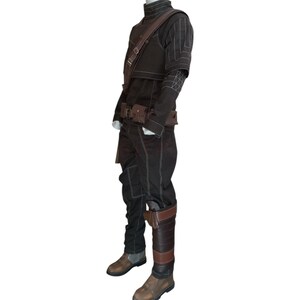 May include: A brown costume with white stitching, featuring a high-collared jacket, pants, and a belt with pouches. The outfit includes a shoulder strap and brown leather boots. The costume is displayed on a mannequin.
