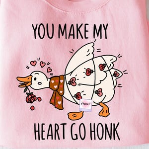 May include: Pink sweatshirt with the text "YOU MAKE MY HEART GO HONK" and a cartoon goose design. The goose has a scarf and roses. The sweatshirt is a crew neck style.