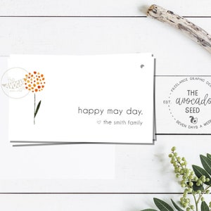 Puede incluir: Una tarjeta blanca con una ilustración de una flor naranja y amarilla y el texto "happy may day. the smith family". La tarjeta tiene un sello gris con el texto "THE avocado SEED EST. 2012 SEVEN DAYS A WEEK".