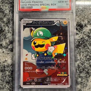 May include: A graded Pokémon card featuring Luigi Pikachu from the 2016 P.M. JPN. XY PROMO set. The card has a colourful illustration of Pikachu dressed as Luigi, with text in Japanese and English. The card is graded GEM MT 10.