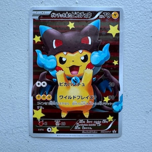 Puede incluir: Una carta coleccionable de Pokémon con Pikachu con un disfraz marrón oscuro y azul. La tarjeta tiene texto japonés y un personaje Pikachu amarillo con una expresión feliz. La tarjeta tiene un fondo rojo y dorado con detalles de estrellas.