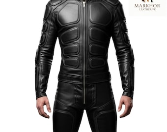 May include: Black leather jacket and pants set. The jacket features a stand-up collar, a front zipper, and padded panels on the shoulders, chest, and arms. The pants have matching padded details. The logo "MARKHOR LEATHER PK" is in the upper right corner.