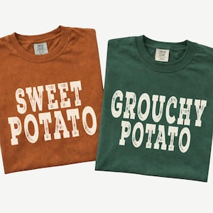 May include: Two crew neck t-shirts, one in burnt orange and one in dark green. The orange shirt features the white text SWEET POTATO, and the green shirt features the white text GROUCHY POTATO. Both shirts have a Comfort Colors brand neck label.