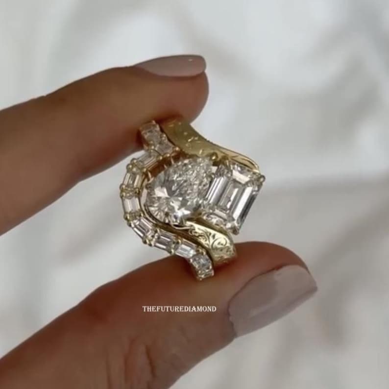 Op de afbeelding: Een driedelige gouden ringenset met een grote ovaal geslepen diamant, een smaragd geslepen diamant en baguette-geslepen diamanten. De ringen hebben een wervelend ontwerp en worden tussen de vingers gehouden. De tekst "THEFUTUREDIAMOND" is zichtbaar.