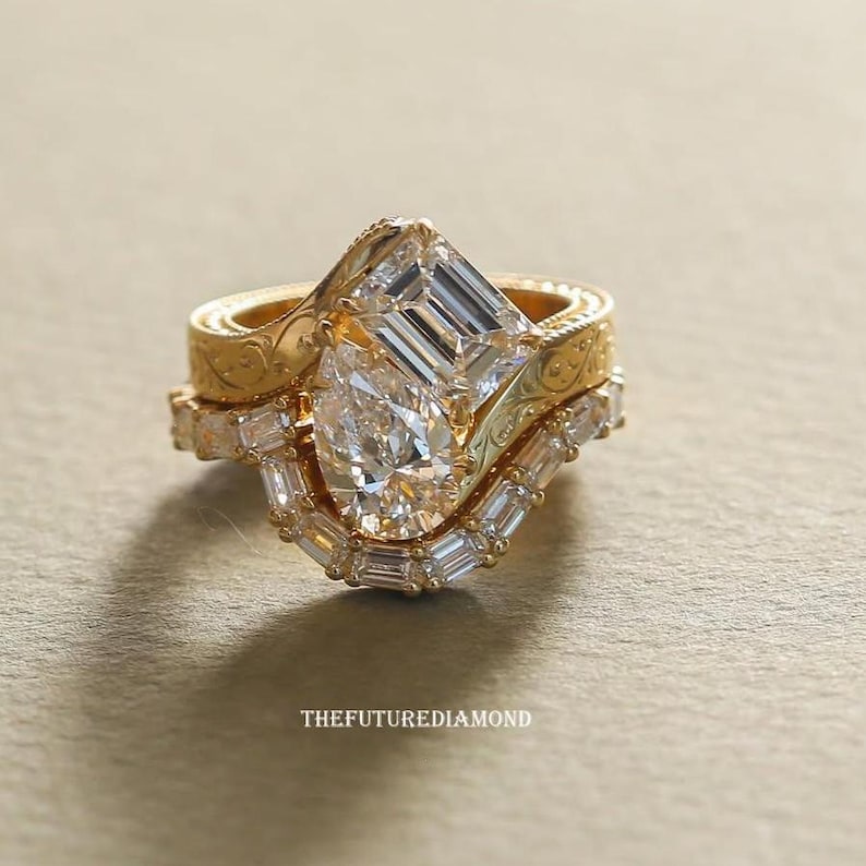 Op de afbeelding: Een set van drie gouden ringen met ingewikkelde details. De ringen hebben een peervormige diamant, een smaragdgeslepen diamant en verschillende kleinere diamanten. De ringen zijn op elkaar gestapeld, wat een unieke en elegante uitstraling cre&euml;ert. De tekst "THEFUTUREDIAMOND" staat onderaan.