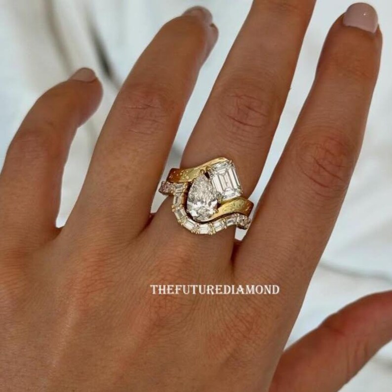 Op de afbeelding: Een gouden en diamanten ring set met een peervormige diamant als middensteen, geflankeerd door smaragd- en baguette-diamanten. De ring heeft een uniek, gebogen ontwerp met de tekst "THEFUTUREDIAMOND".