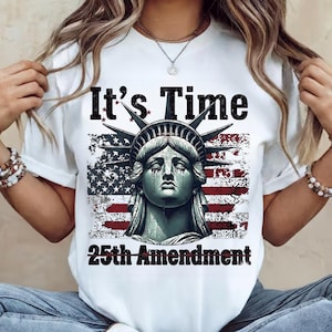 May include: White t-shirt featuring a graphic of the Statue of Liberty with the American flag in the background. The text "It's Time" and "25th Amendment" are printed on the shirt in black.