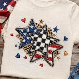 Op de afbeelding: Crèmekleurig T-shirt met drie sterontwerpen. Eén ster heeft een blauw-wit patroon, een andere een zwart-wit geblokt patroon en de derde een rood-wit gestreept patroon. Het shirt heeft een luipaardprint achtergrond met kleine ster- en hartaccenten.