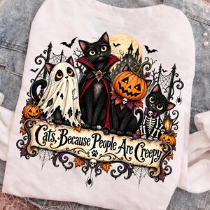 Peut inclure: Un t-shirt blanc avec un motif représentant quatre chats noirs en costumes d'Halloween, dont un fantôme, un vampire, une citrouille et un squelette. Sous les chats, une bannière affiche le texte : "Cats, Because People Are Creepy."