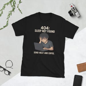 May include: Black t-shirt with the text "404: SLEEP NOT FOUND" above an illustration of a tired person using a laptop. Below the illustration, the text reads "SEND HELP. AND COFFEE."