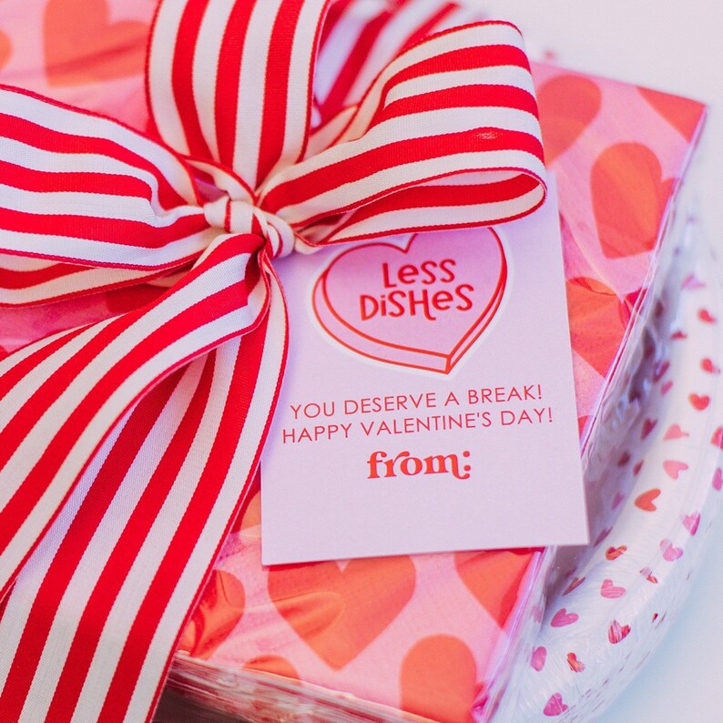 May include: A gift wrapped in red and white striped ribbon with a pink and white card that says "Less Dishes" and "You deserve a break! Happy Valentine's Day! from:". The gift is wrapped in pink napkins with red hearts.