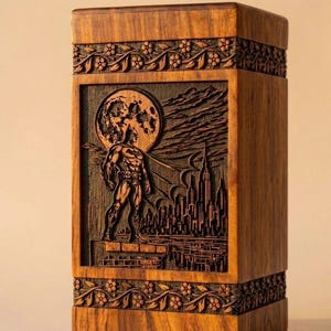 May include: A wooden box with a carved Batman scene. The artwork depicts Batman standing in front of a cityscape with a full moon. The box has floral carvings around the top and bottom.