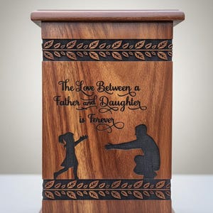 Può includere: Urna in legno dalla forma rettangolare e finitura in legno scuro. La parte anteriore presenta la scritta "The Love Between a Father and Daughter is Forever" con sagome di padre e figlia. Motivi decorativi a foglie intagliati nel legno.