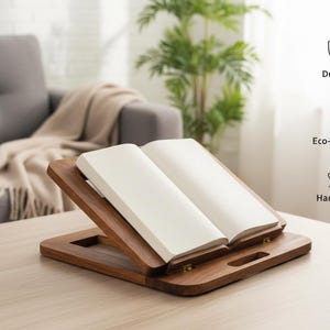Könnte beinhalten: Ein hölzerner Buchständer mit einem offenen Buch. Der Ständer ist aus dunklem Holz gefertigt und hat eine rechteckige Basis mit einem Griff. Das Buch hat weiße Seiten. Der Ständer ist als langlebig, umweltfreundlich und handgefertigt gekennzeichnet.