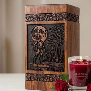 May include: A wooden box with a carved Batman scene, featuring the superhero standing before a cityscape and a full moon. The box is next to a lit red candle with rose petals and the text "VENUSTAS ROSE & SANDALWOOD".