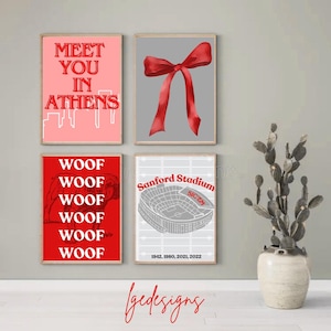 May include: Four framed art prints with red and grey designs. One print says "Meet You In Athens", another features a red bow, a third says "Woof" repeatedly, and the last shows a stadium with the text "Sanford Stadium".