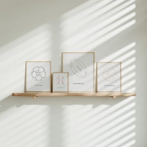 May include: Four framed prints with black and white line drawings of different sports balls. The prints are on a wooden shelf against a white wall. The text on the prints reads "United in Christ", "Never Change Who You Are", "Endure with Faith", and "Navigate Through Faith".