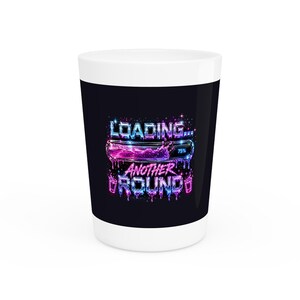 May include: A white ceramic coffee mug with a black band featuring the text "LOADING... ANOTHER ROUND" in a neon-style font. The design includes a loading bar with 75% progress and splashes of pink and blue.