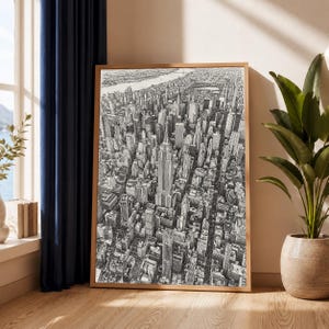 Op de afbeelding: Een zwart-witte lijntekening van een dicht stedelijk landschap met een prominente wolkenkrabber in het midden, omringd door talloze gebouwen en straten, alles ingelijst in een eenvoudige rechthoekige houten lijst.