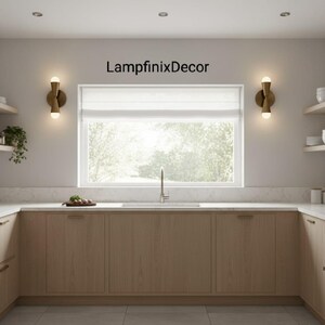 May include: A contemporary kitchen featuring light wood cabinets, a white worktop, and a large window. Two gold wall lights with spherical bulbs are positioned either side of the window. The text "LampfinixDecor" is above the window.