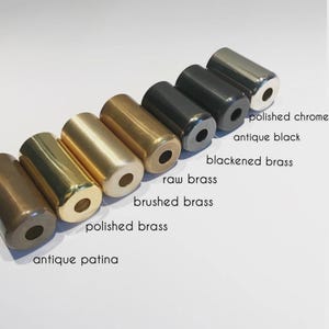 May include: An assortment of cylindrical metal objects in different finishes, such as polished chrome, antique black, and polished brass. The image showcases a variety of colours and textures, with labels indicating each finish. The objects are arranged in a line.