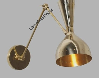 Pode incluir: Uma luminária de parede em latão com um braço ajustável e uma cúpula cónica. A cúpula tem pequenas perfurações e um interior quente e dourado. A luminária é montada numa base circular. O texto "LampfinixDecor" é visível.