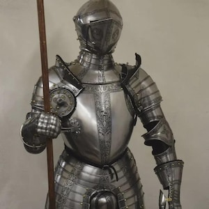 May include: A full suit of polished steel armor, complete with a helmet, chest plate, and articulated limbs. The armor is adorned with decorative etchings and rivets. A wooden spear is held in the right hand, suggesting a medieval or historical theme.