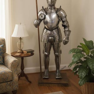 May include: A full suit of medieval armor made of polished metal, standing on a wooden base. The armor includes a helmet, chest plate, and leg protection. It holds a long wooden spear. The suit is a decorative item.