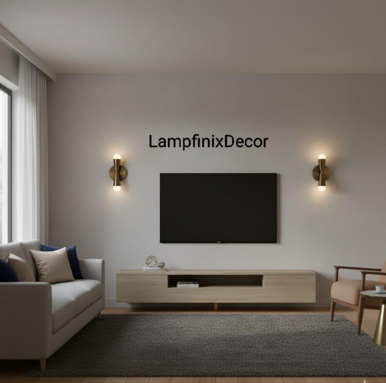 May include: A contemporary living room featuring a light grey sofa, a wooden entertainment unit, and a large black television. Two gold sconces with round bulbs are positioned either side of the TV. The text "LampfinixDecor" is printed on the wall.