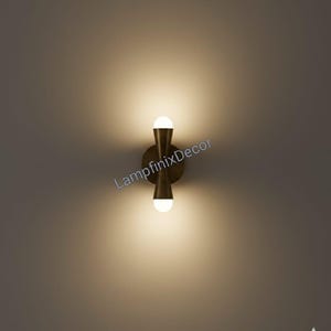 May include: A contemporary wall light with a brass finish, featuring two spherical light bulbs. The fixture has a distinctive hourglass shape and is mounted on a circular base. The text "LampfinixDecor" is visible on the image.