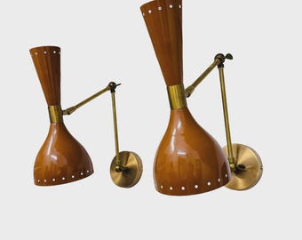 May include: Two mid-century modern wall sconces. Each sconce features a brown, cone-shaped shade with white dot accents, a brass-colored arm, and a circular wall mount. The shades have a glossy finish.