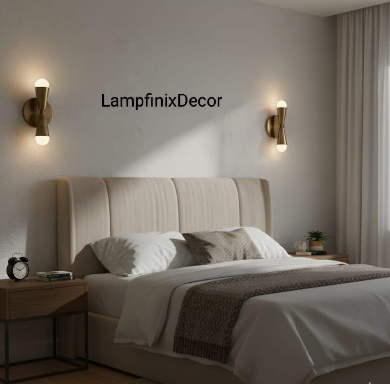 May include: A bedroom scene featuring two brass wall sconces with glowing bulbs. The beige headboard and white bedding are visible. A brown throw and the text "LampfinixDecor" on the wall complete the scene.