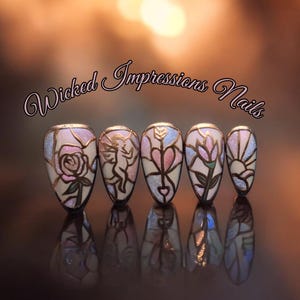 Puede incluir: Conjunto de cinco uñas postizas con diseños intrincados. Cada uña presenta un diseño diferente, incluyendo una rosa, un ángel, un corazón, una flor y un sol, todos delineados en dorado. El texto "Wicked Impressions Nails" está en la parte superior.