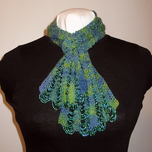 May include: A green and blue beaded scarf with a lacy knit pattern. The scarf is tied around a black shirt.