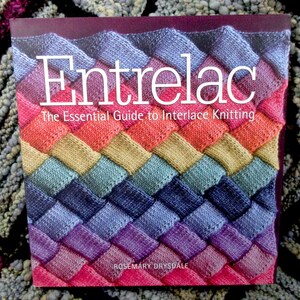 May include: A book titled "Entrelac" with the subtitle "The Essential Guide to Interlace Knitting" by Rosemary Drysdale. The cover features a colorful, woven-like pattern in shades of pink, orange, yellow, green, blue, and purple.