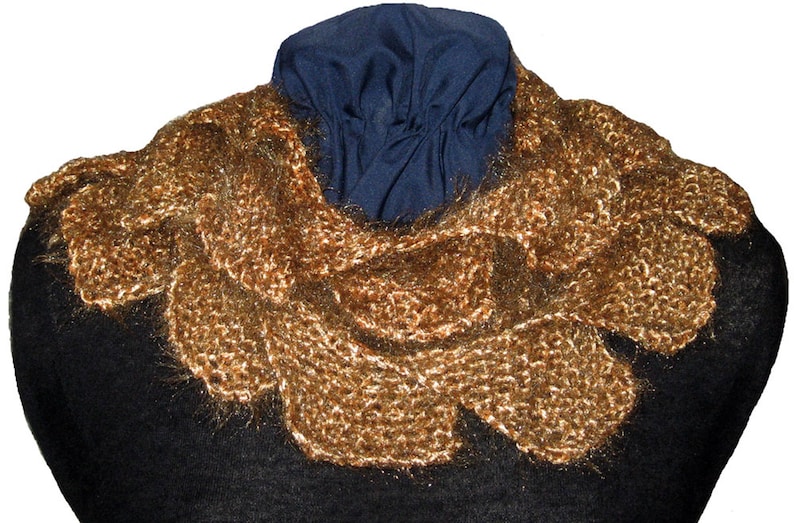 May include: A gold knitted scarf with a fluffy texture. The scarf is draped over a black mannequin.