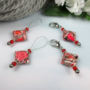May include: Four red and white marbled stitch markers with silver metal clasps and loops. Two markers have silver metal clasps and two have silver metal loops.
