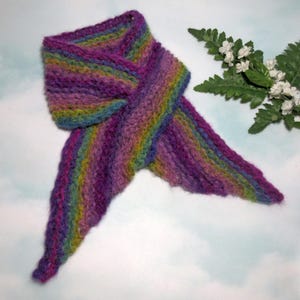 May include: A hand-knitted scarf in a spectrum of colors, including purple, blue, green, and yellow. The scarf is made of a soft, textured yarn and has a unique, asymmetrical design. The scarf is approximately 60 inches long.