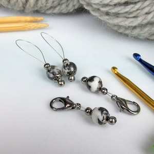 May include: Two silver stitch markers with black and white marbled beads and two silver stitch markers with a silver clasp and black and white marbled beads.