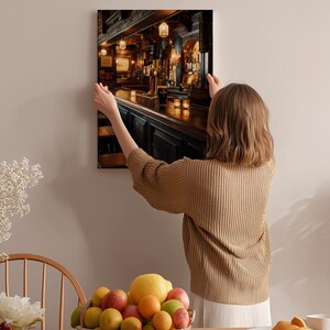 A woman hangs a framed picture of a bar on a wall in a cozy, homely setting.