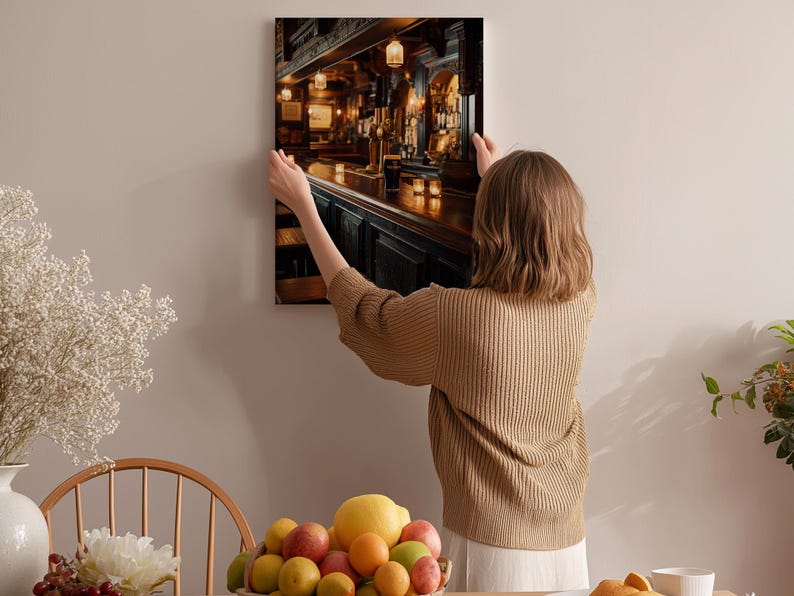 A woman hangs a framed picture of a bar on a wall in a cozy, homely setting.